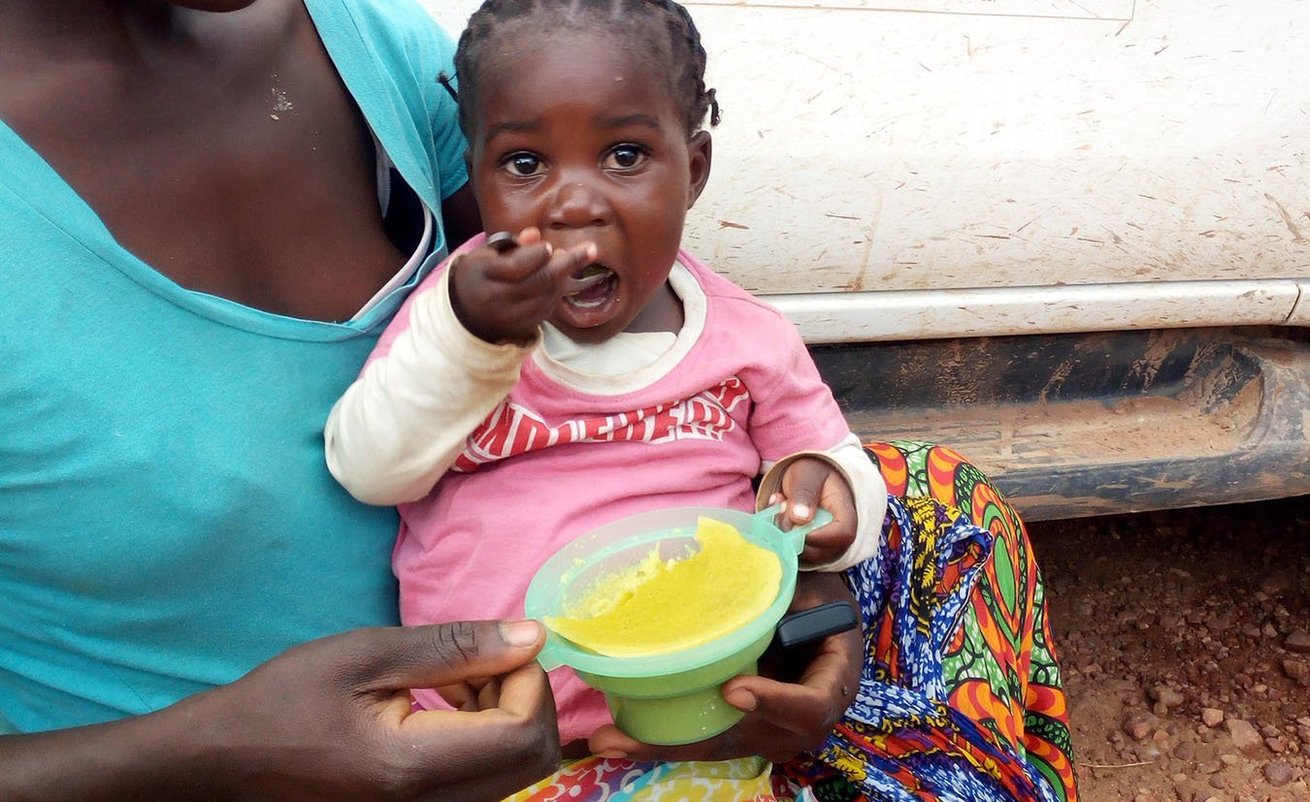 Little Mildred enjoying orange maize-pumpkin leaves porridge from a CARE food demonstration in Zambia.