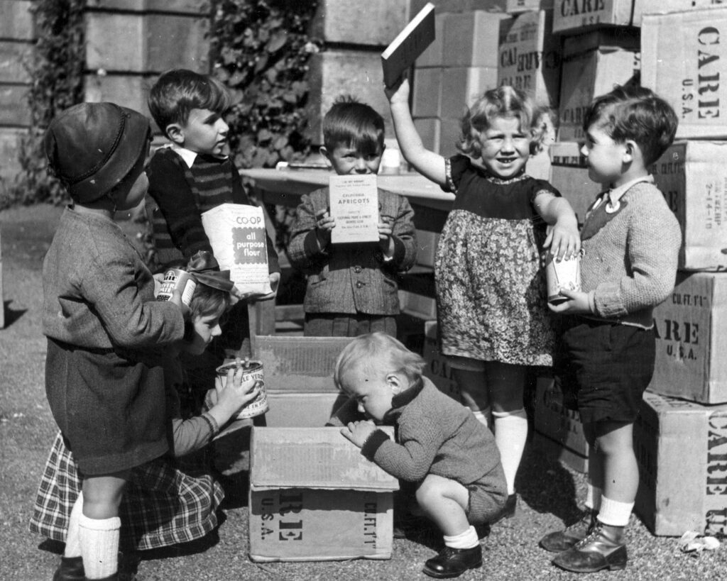 Young boys and girls displaying contents of CARE food package in Europe. July 1948.