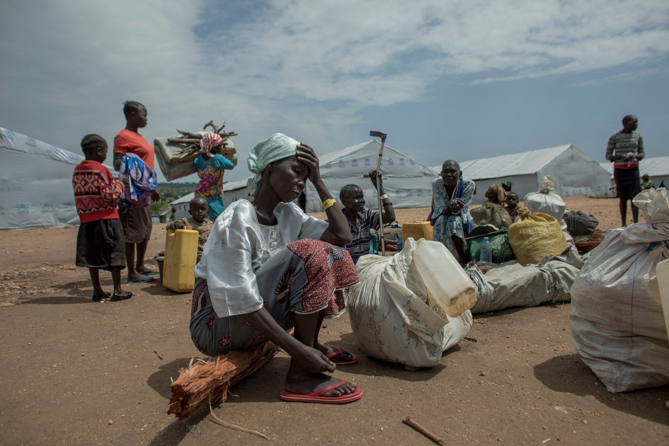 Refugees, carrying their few remaining possessions, wait in the transportation area of the Imvepi Refugee Settlement in Uganda in 2019