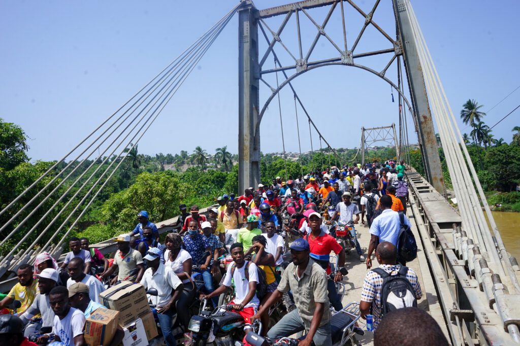 People photographed on and near the Dumarsais Estime bridge, where pedestrians and some smaller vehicles can pass, but not truck, in late August, 2021, after a 7.2 earthquake wrecked havoc in Haiti. The bridge connects the town of Jèrèmie to the rest of the country's highways. © 2021 CARE
