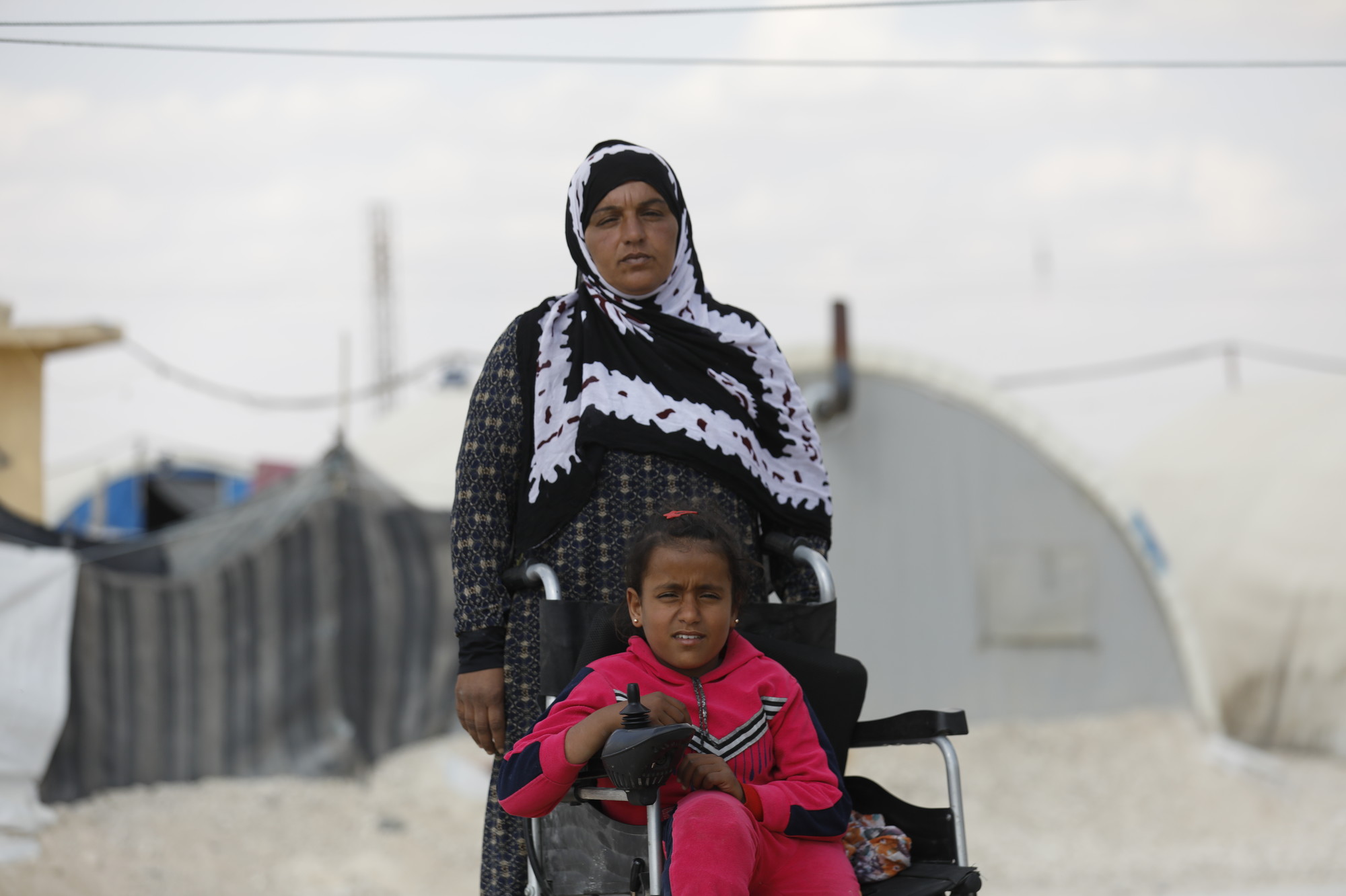 A young girl, Bushra who is in a wheelchair, pictured with her mother in an informal settlement for displaced persons. Photo: Delil Souleiman/CARE