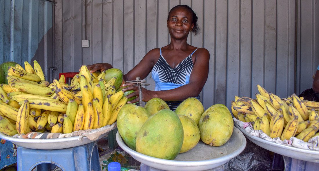 A woman works at a fruit stand. Around her are bowls of bright yellow fruit.