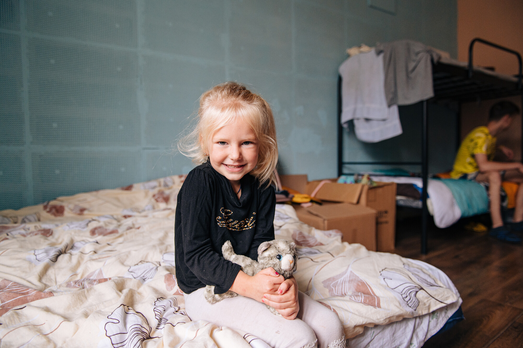 A young girl, Kristina, sits in a bad and holds a stuffed animal she brought with her when she fled her home in Ukraine.