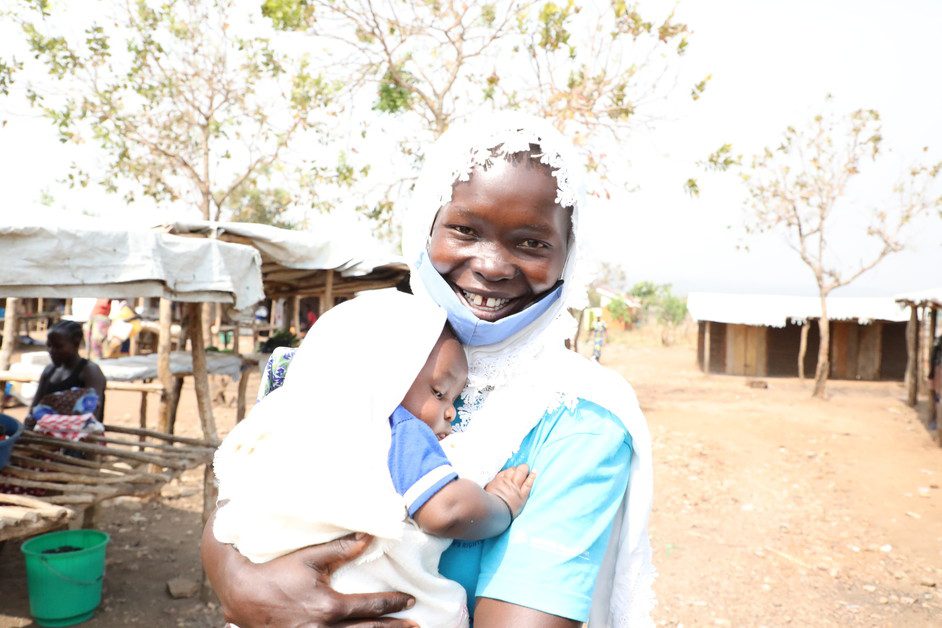 A woman smiles as she holds a baby