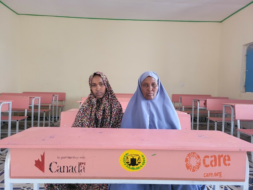 A young woman sits at a desk in a classroom beside her mother