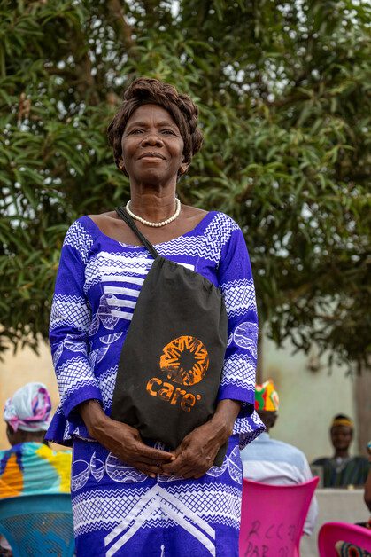 A woman stands proudly smiling and holding a bag with CARE's logo on it