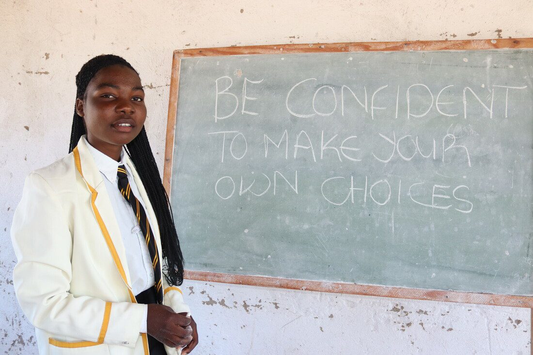 A teenage girl stands beside a chalkboard