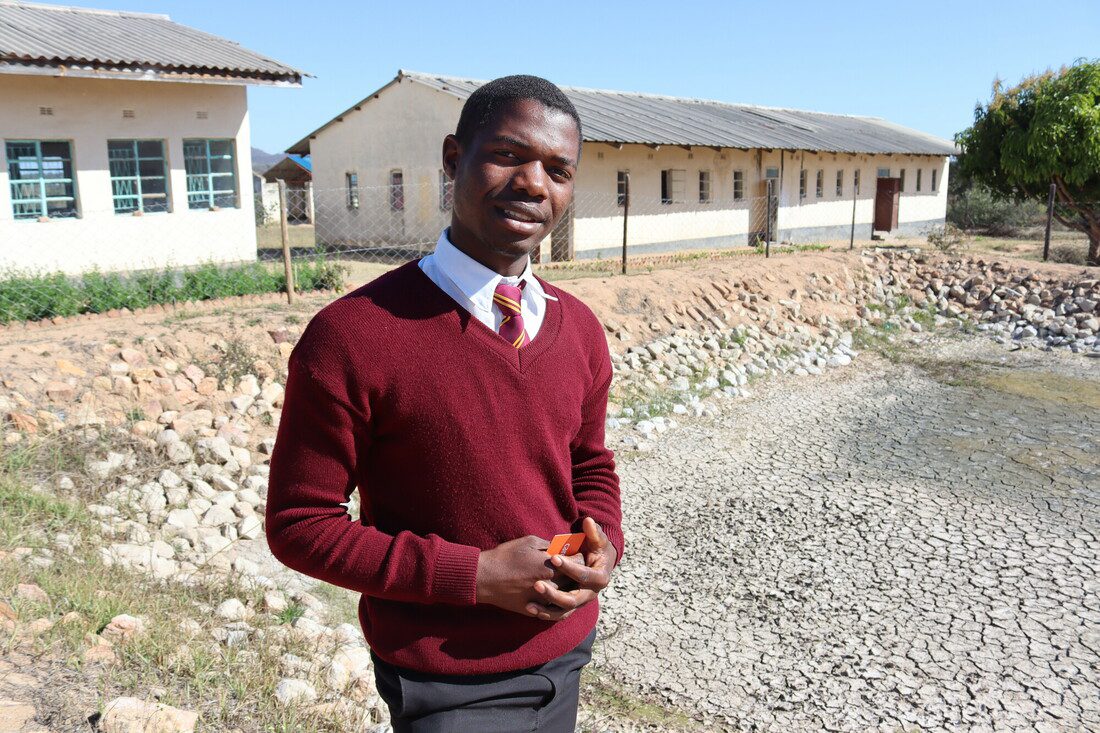 A young man stands outdoors in front of a school building