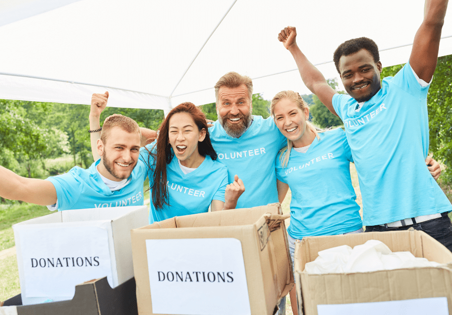 Five people stand together excitedly raising their arms behind donation boxes.