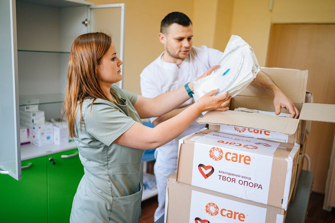 A woman and man wearing scrubs unpack items from boxes that have CARE and our partner Tvoya Opora's logos on them