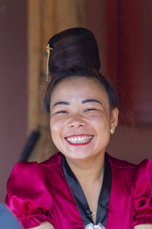 A close up photo of a woman smiling, looking at the camera, with the traditional "high bun."