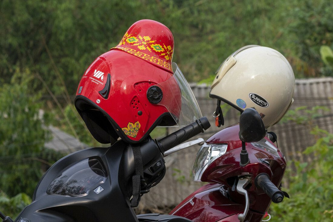A close up photo of two motorcycle helmets resting on top of 2 bikes. One is standard in shape and the other has been designed to fit the 6 inch buns.