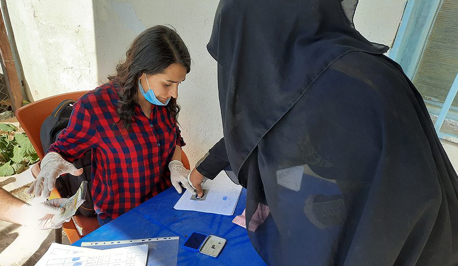 A woman sits at a table holding at a document while another women stands and adds her thumbprint to the document.