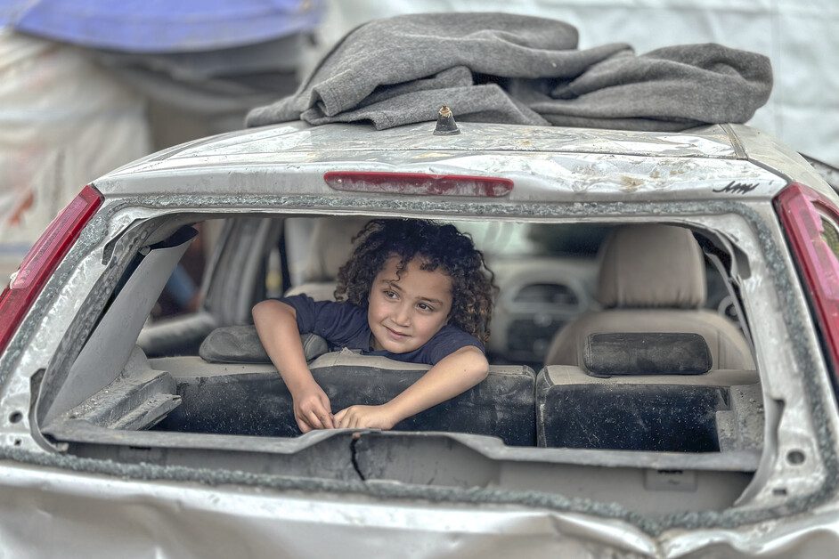Un enfant est assis dans une voiture partiellement détruite que sa famille utilise en guise d’abri dans le camp de réfugiés de Nuseirat, à Gaza. Grayscale Media, 2023/CARE