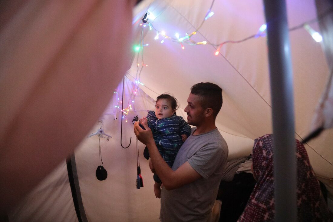 A man holds a baby inside a tent and put up small strings of coloured lights