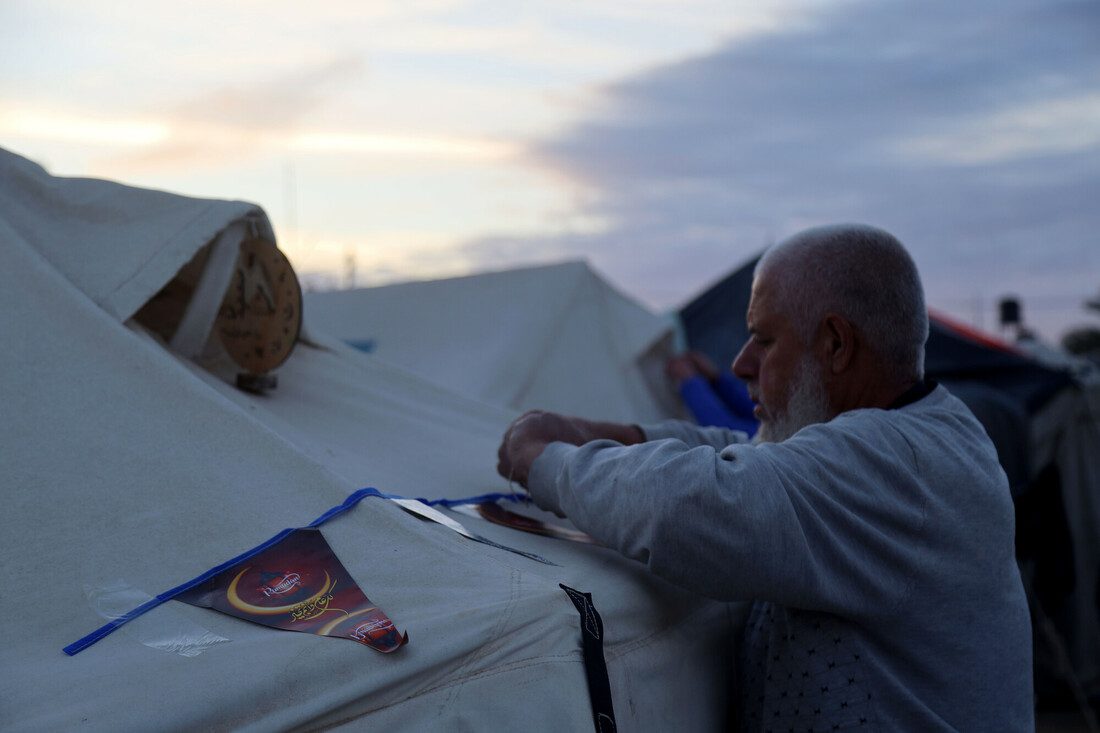 A man attaches a homemade banner to a tent in a displaced persons camp.