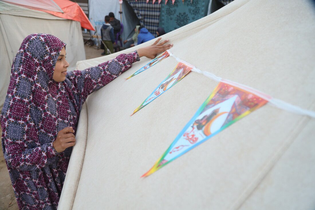 A woman attaches a homemade banner to a tent in a displaced persons camp.
