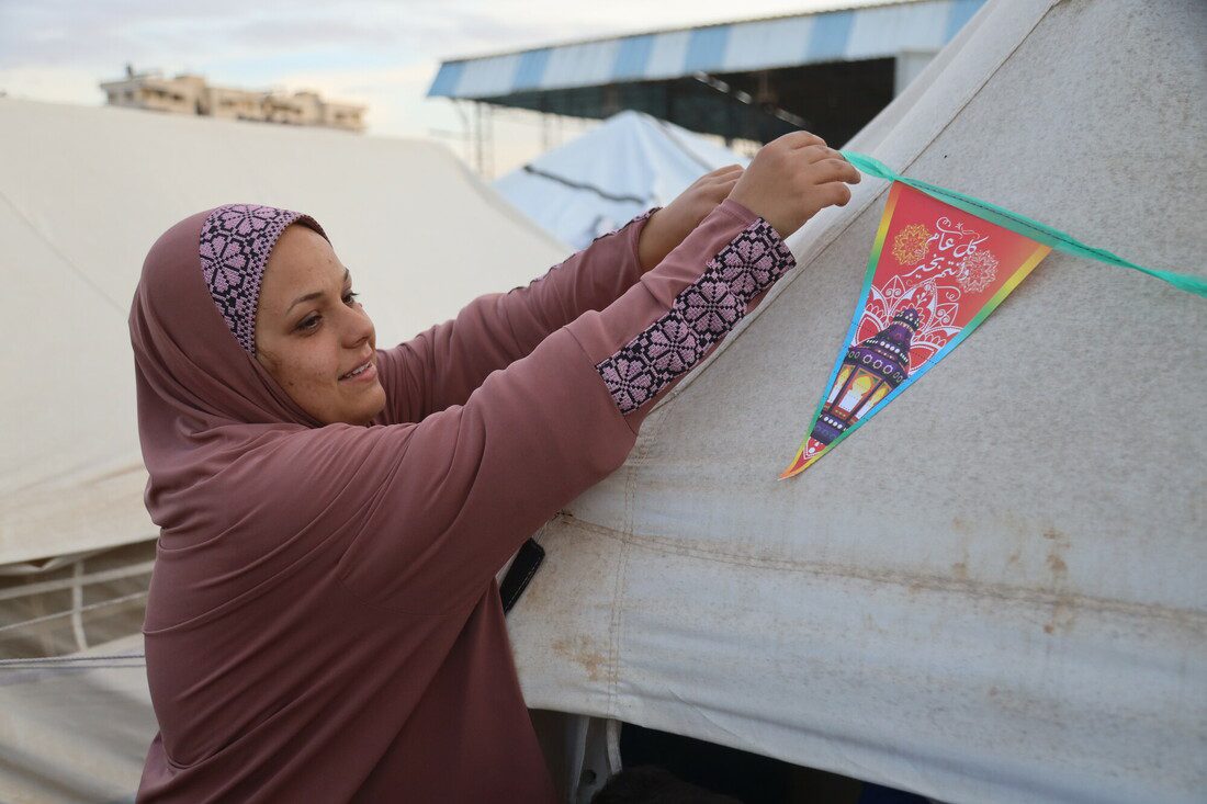 A woman attaches a homemade banner to a tent in a displaced persons camp.
