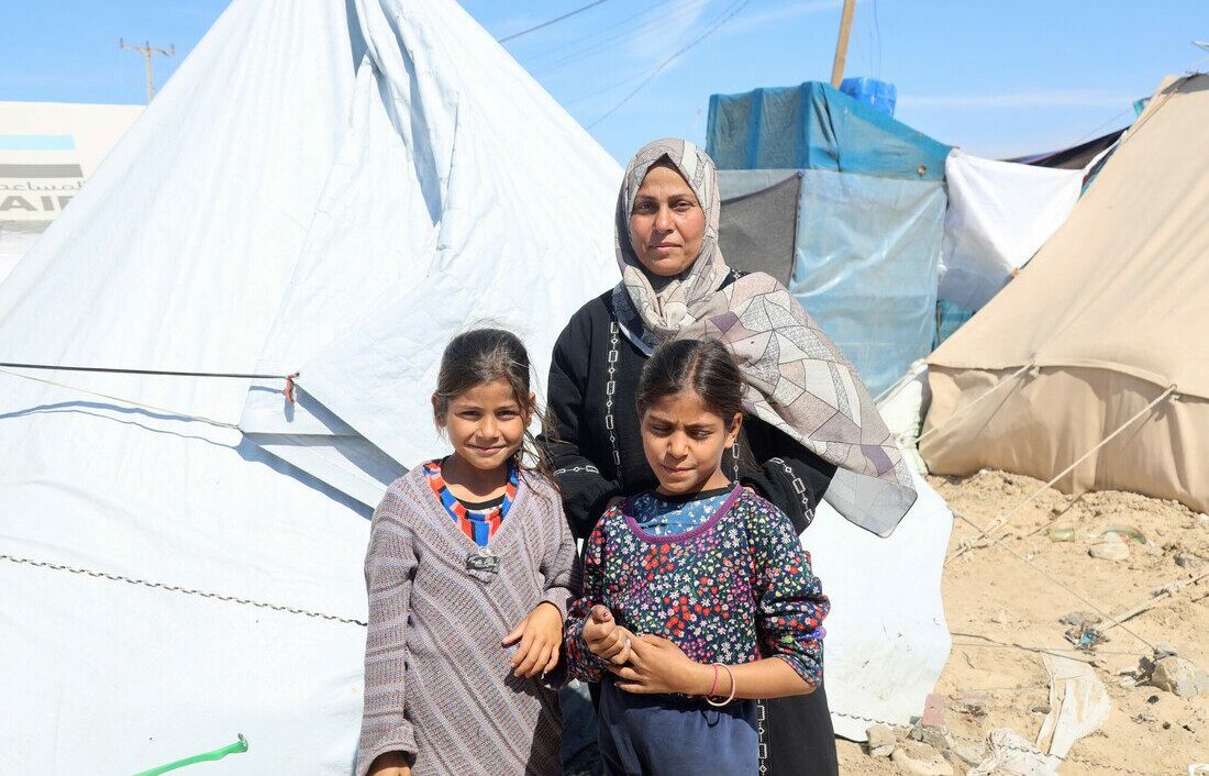 A woman and two of her daughters stand in front of a white tent.
