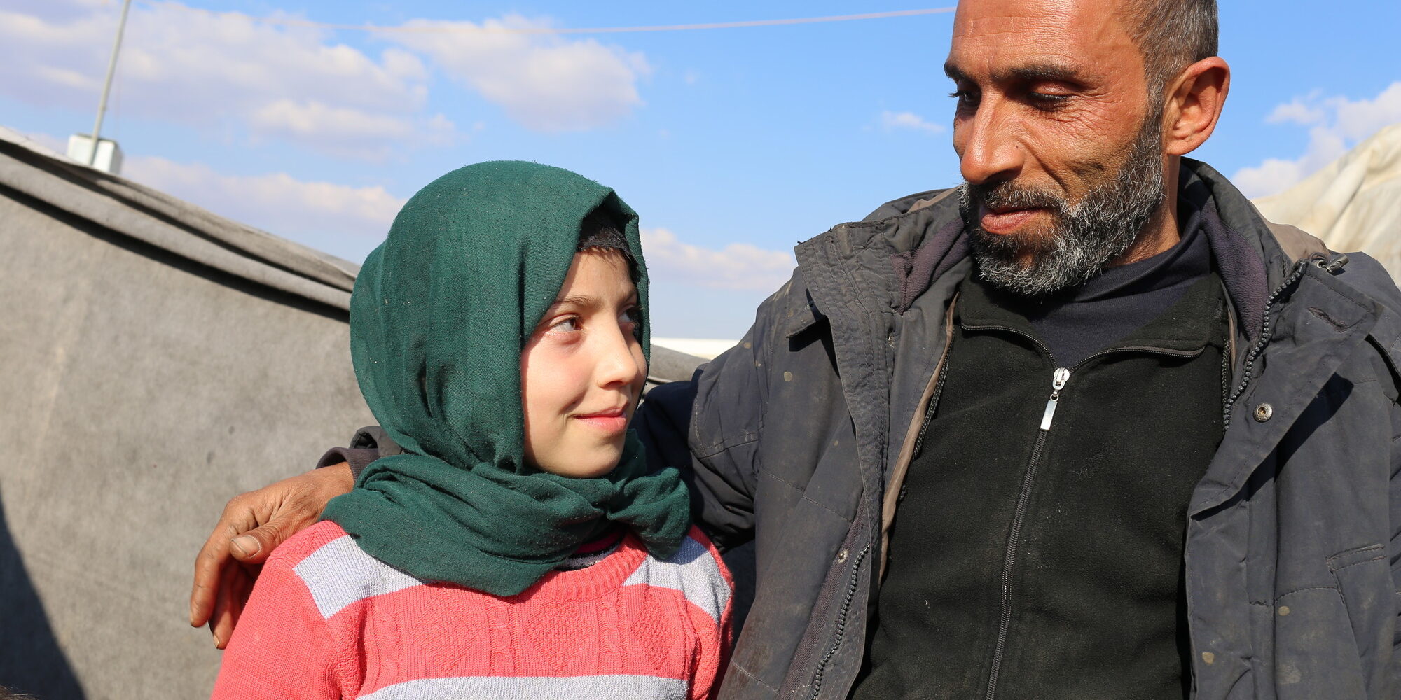 A young girl, Amra, stands with her father in a displaced persons camp. Photo: Tarek Satea/CARE