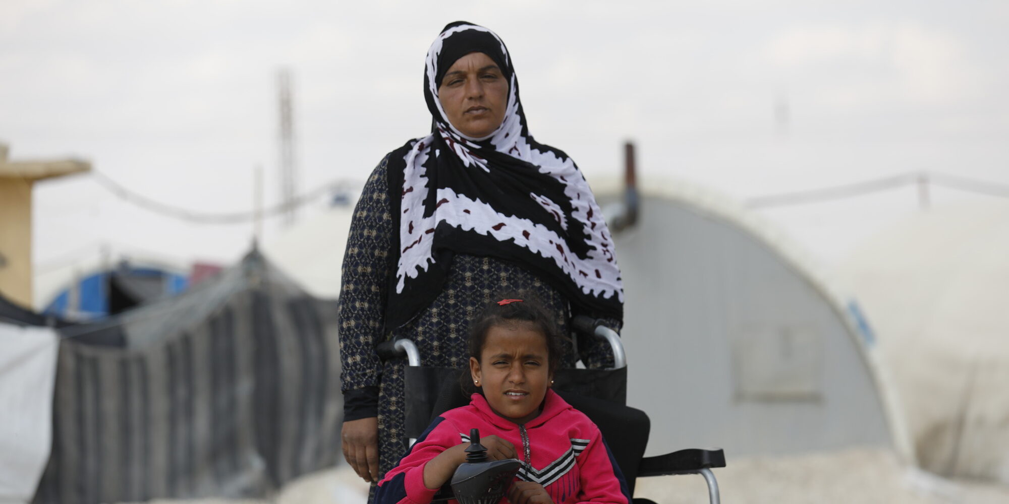 A young girl, Bushra who is in a wheelchair, pictured with her mother in an informal settlement for displaced persons. Photo: Delil Souleiman/CARE